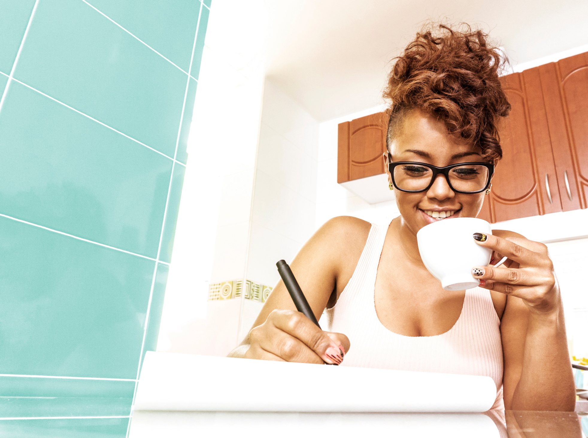Inspired black woman writing on notepad while enjoying a cup of coffee smiling